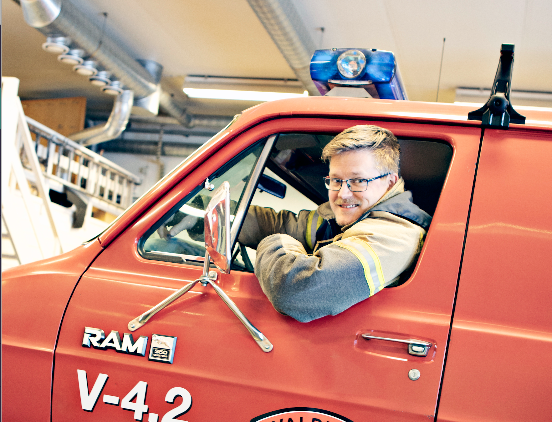 Brannkonstabel sitter i bil og kikker ut vinduet med et smil